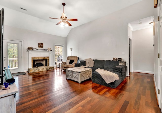 living room with dark wood-type flooring, a wealth of natural light, vaulted ceiling, and a stone fireplace