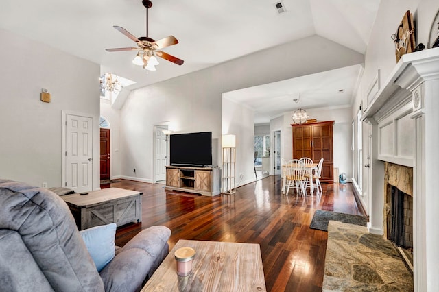 living room with ornamental molding, ceiling fan with notable chandelier, high vaulted ceiling, a stone fireplace, and dark wood-type flooring