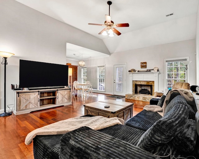 living room featuring ceiling fan, vaulted ceiling, a stone fireplace, and hardwood / wood-style flooring