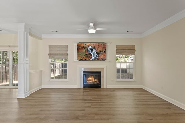 unfurnished living room featuring wood-type flooring, crown molding, ornate columns, a tiled fireplace, and ceiling fan