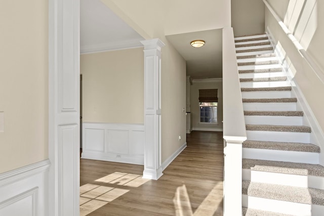 stairway with hardwood / wood-style floors, crown molding, and decorative columns