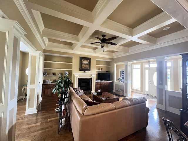 living room featuring dark wood-type flooring, built in shelves, coffered ceiling, ornamental molding, and ceiling fan