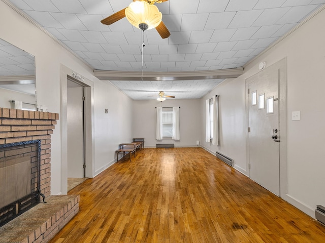 unfurnished living room featuring baseboard heating, hardwood / wood-style floors, a fireplace, and ornamental molding