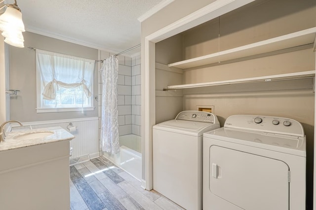 laundry area featuring a textured ceiling, sink, washing machine and clothes dryer, crown molding, and light hardwood / wood-style flooring