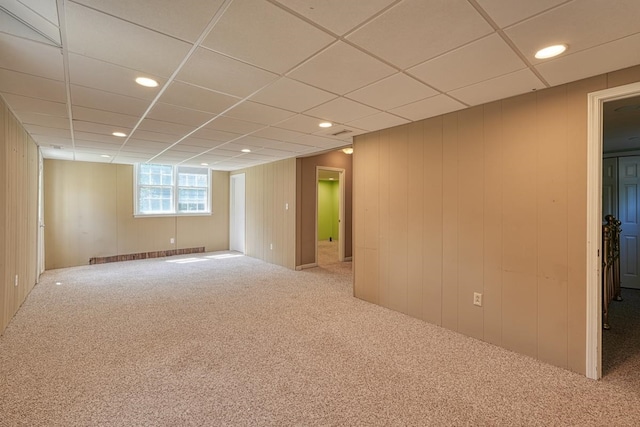 carpeted empty room with a paneled ceiling and wooden walls