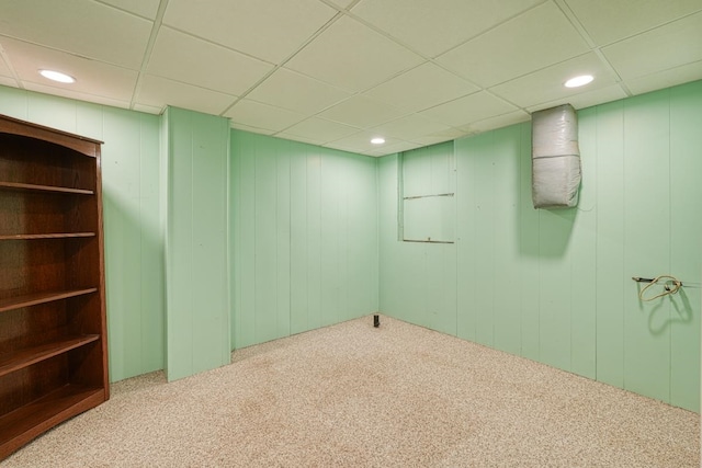 carpeted empty room with wood walls and a drop ceiling