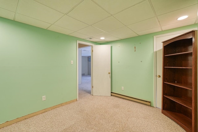 empty room with a paneled ceiling, light colored carpet, and a baseboard heating unit