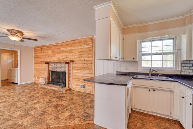 kitchen with a fireplace, white cabinetry, wooden walls, sink, and ceiling fan