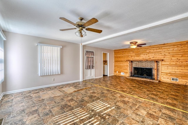 unfurnished living room featuring wood walls, ceiling fan, a healthy amount of sunlight, and a brick fireplace