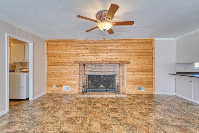 unfurnished living room featuring a textured ceiling, separate washer and dryer, a fireplace, and wooden walls