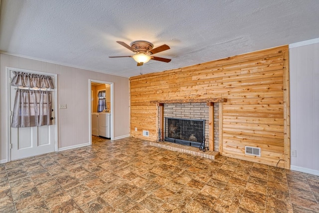 unfurnished living room with a textured ceiling, washer / clothes dryer, wooden walls, a brick fireplace, and ceiling fan