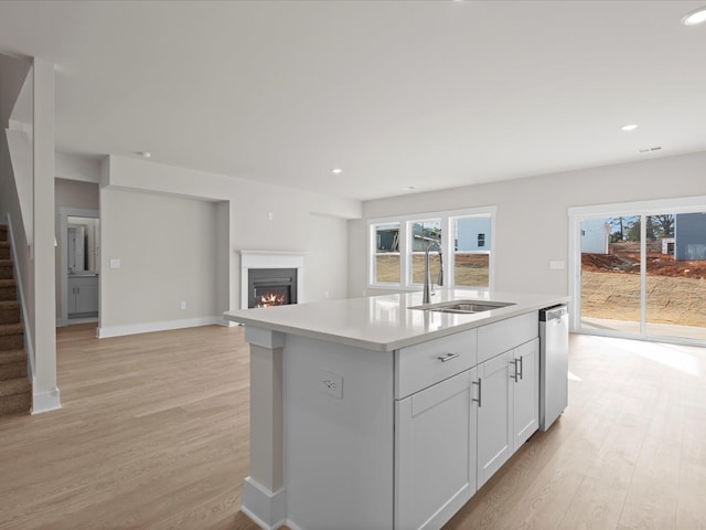 kitchen with sink, white cabinetry, light hardwood / wood-style flooring, dishwasher, and an island with sink