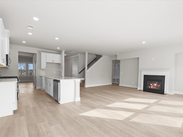 kitchen featuring sink, appliances with stainless steel finishes, a kitchen island with sink, white cabinetry, and light wood-type flooring