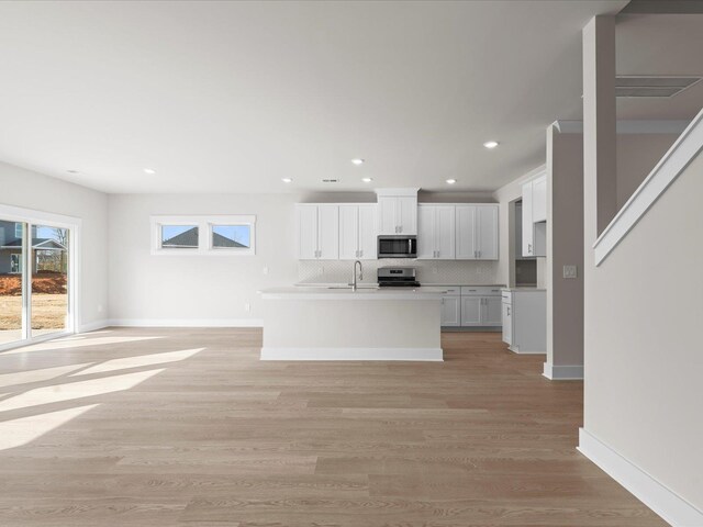 kitchen with white cabinets, decorative backsplash, a kitchen island with sink, light hardwood / wood-style floors, and stainless steel appliances