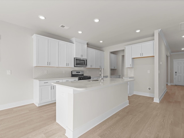 kitchen featuring light hardwood / wood-style flooring, stainless steel appliances, white cabinets, and a center island with sink