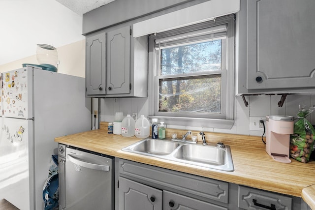 kitchen featuring gray cabinetry, sink, stainless steel dishwasher, and white refrigerator