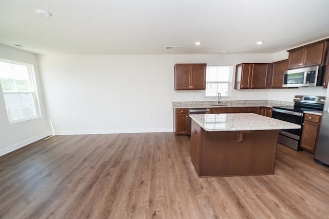 kitchen with dark hardwood / wood-style flooring, a center island, sink, light stone countertops, and appliances with stainless steel finishes