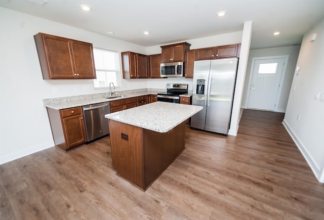 kitchen featuring sink, light stone counters, appliances with stainless steel finishes, hardwood / wood-style floors, and a kitchen island