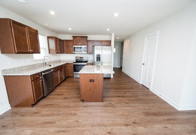 kitchen with stainless steel appliances, light hardwood / wood-style floors, sink, light stone counters, and a center island