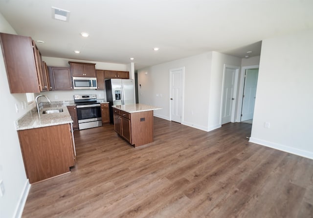 kitchen with stainless steel appliances, dark wood-type flooring, a center island, sink, and light stone countertops