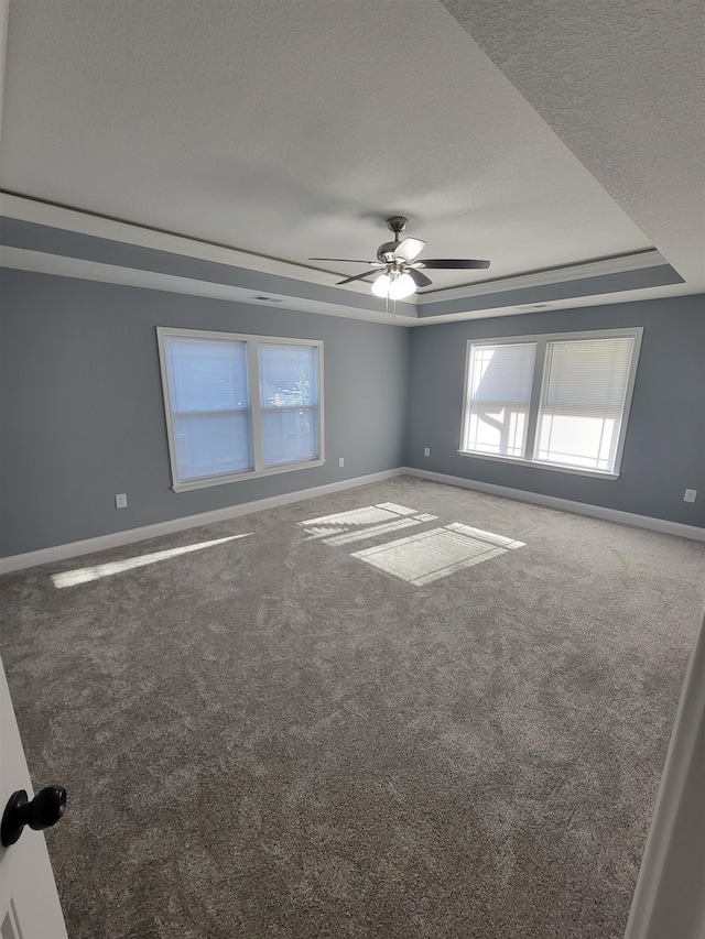 empty room featuring a tray ceiling, carpet, a textured ceiling, and ceiling fan