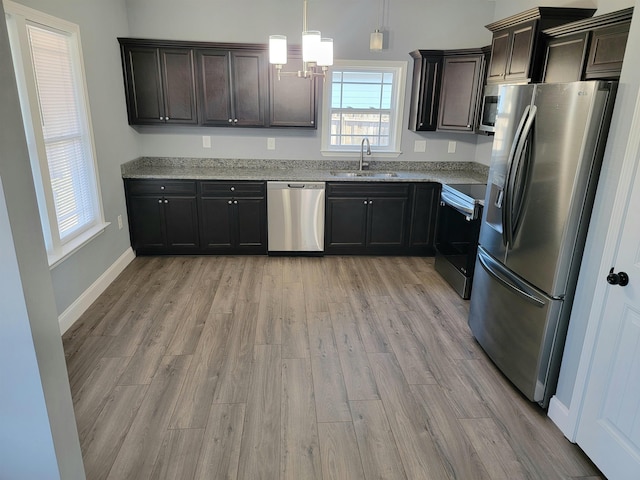 kitchen with appliances with stainless steel finishes, light stone countertops, hanging light fixtures, sink, and light hardwood / wood-style flooring