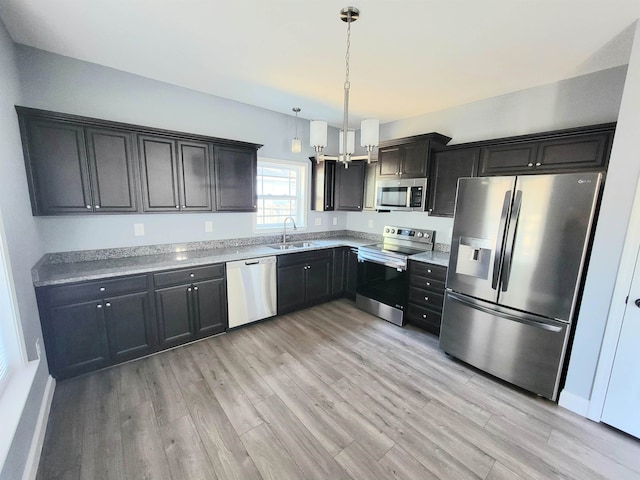 kitchen with stainless steel appliances, sink, light stone counters, hanging light fixtures, and light wood-type flooring