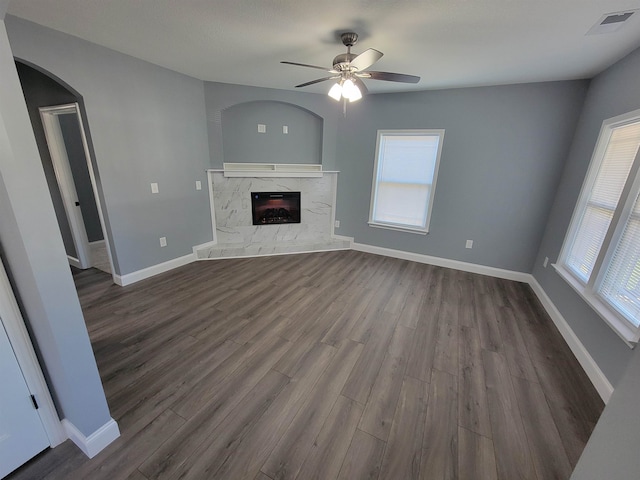 unfurnished living room featuring dark wood-type flooring, a wealth of natural light, a high end fireplace, and ceiling fan