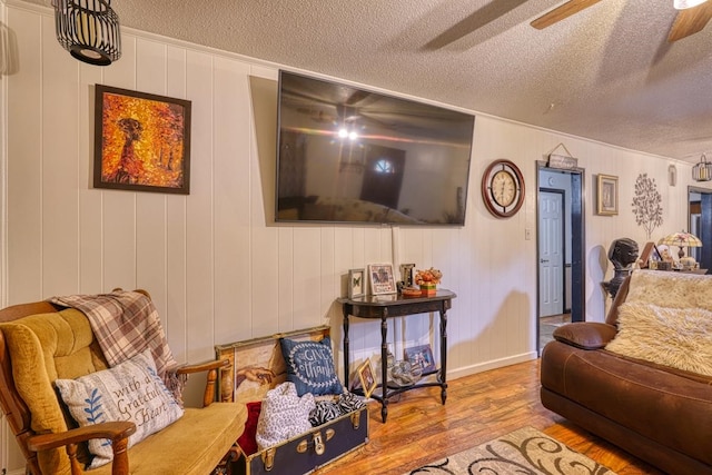 living room featuring ceiling fan, wooden walls, a textured ceiling, and hardwood / wood-style flooring