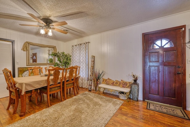 dining space featuring ceiling fan, wood walls, wood-type flooring, and a textured ceiling