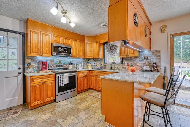 kitchen featuring kitchen peninsula, appliances with stainless steel finishes, plenty of natural light, and a kitchen breakfast bar