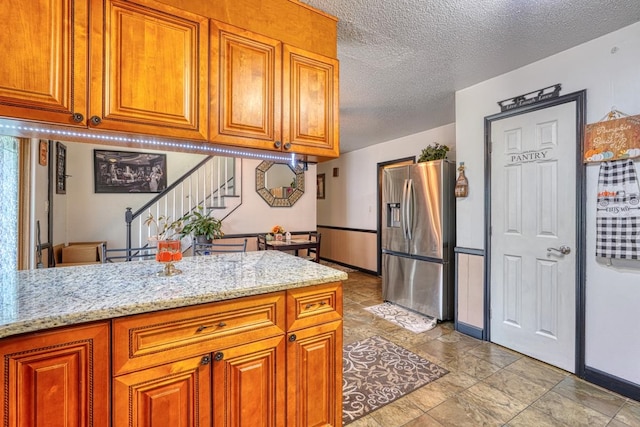 kitchen featuring a textured ceiling, kitchen peninsula, light stone counters, and stainless steel fridge