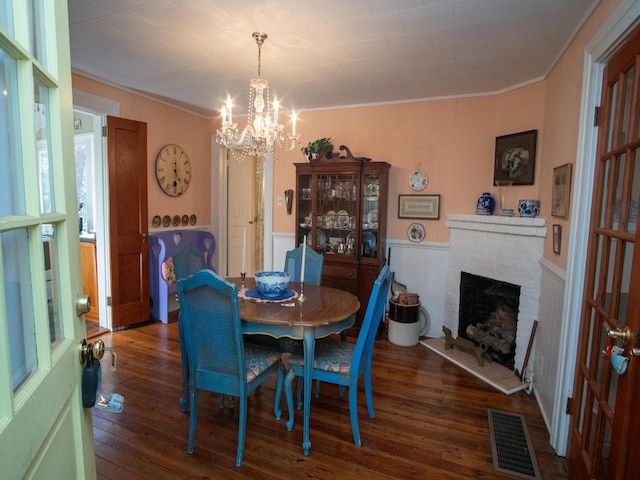 dining area with dark hardwood / wood-style flooring, an inviting chandelier, ornamental molding, and a brick fireplace