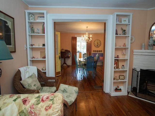 living room featuring a brick fireplace, crown molding, dark hardwood / wood-style floors, and a notable chandelier