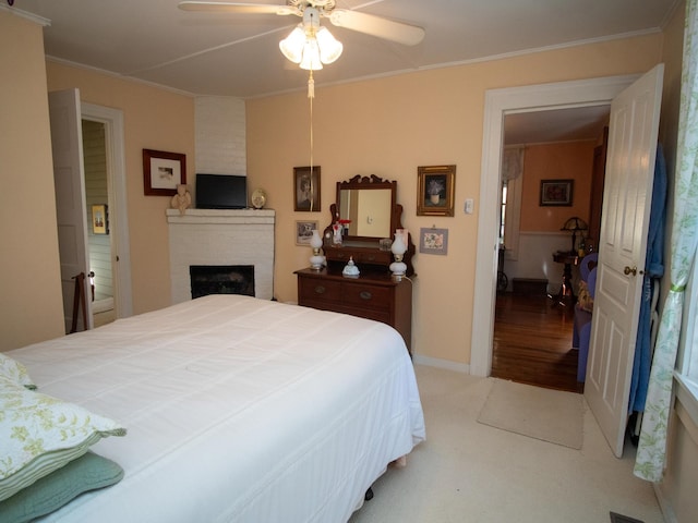 bedroom featuring light hardwood / wood-style flooring, ornamental molding, ceiling fan, and a brick fireplace