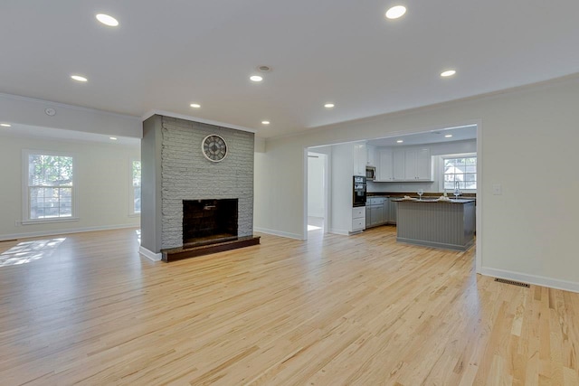 unfurnished living room with light hardwood / wood-style floors, a wealth of natural light, and crown molding