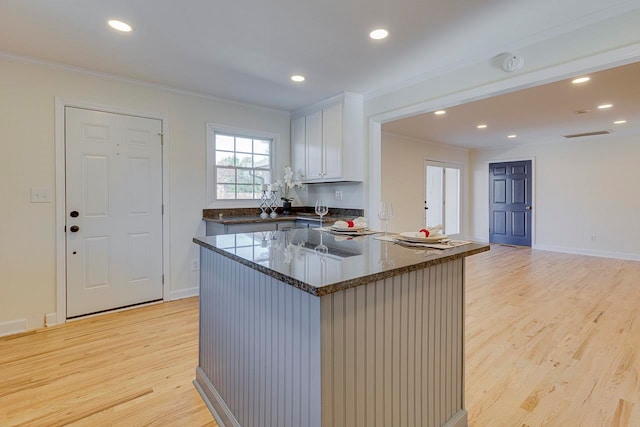 kitchen with white cabinetry, dark stone countertops, ornamental molding, light hardwood / wood-style floors, and kitchen peninsula