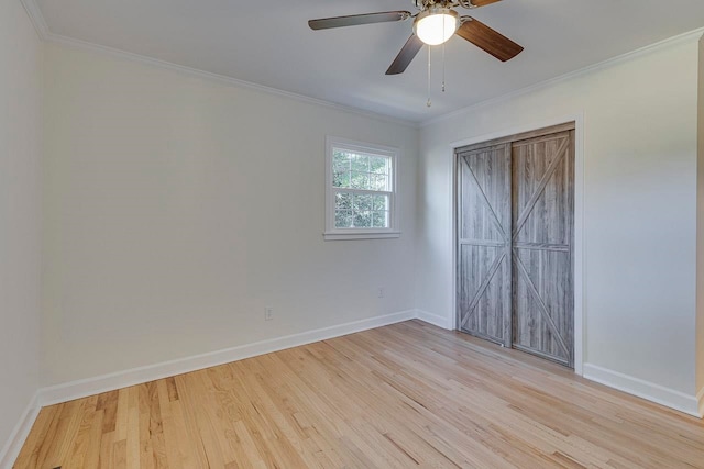 unfurnished bedroom with ornamental molding, ceiling fan, a barn door, light hardwood / wood-style floors, and a closet