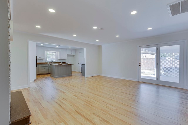 unfurnished living room featuring light wood-type flooring, sink, and ornamental molding