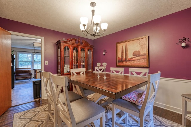 dining space featuring a textured ceiling, baseboards, a notable chandelier, and wood finished floors