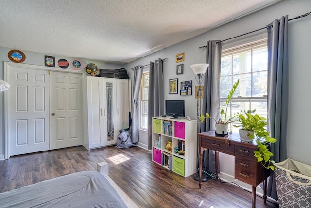 bedroom with a textured ceiling, multiple windows, baseboards, and wood finished floors