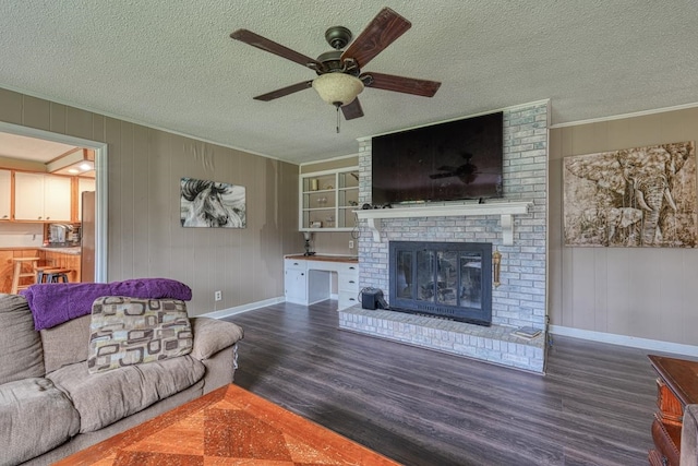 living room featuring a ceiling fan, wood finished floors, a textured ceiling, crown molding, and a fireplace