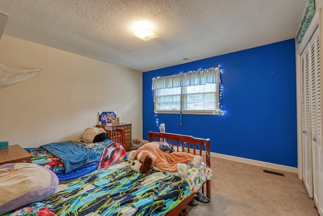 bedroom with baseboards, visible vents, a textured ceiling, carpet floors, and a closet