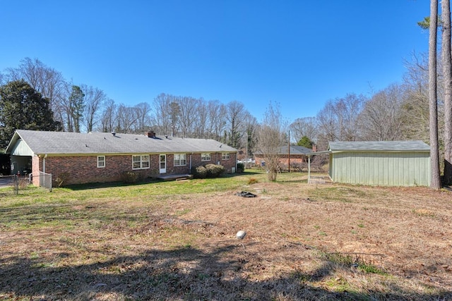 back of house featuring fence, an outdoor structure, a lawn, and brick siding