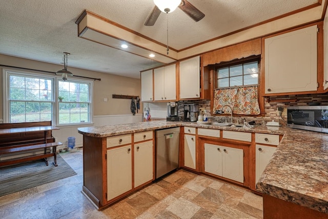 kitchen with a textured ceiling, a wainscoted wall, stainless steel appliances, a peninsula, and a sink