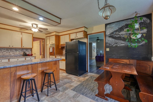 kitchen featuring decorative backsplash, freestanding refrigerator, stone finish floor, ceiling fan, and oven