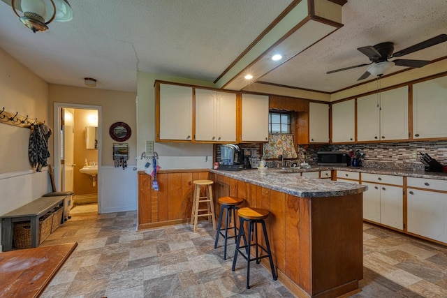 kitchen with stone finish flooring, wainscoting, a textured ceiling, and a kitchen breakfast bar