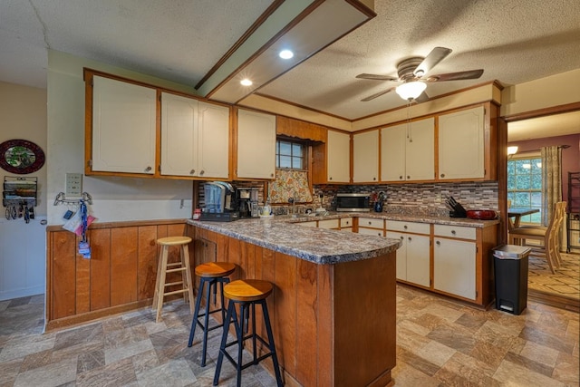 kitchen with stainless steel microwave, a breakfast bar, a peninsula, stone finish flooring, and backsplash