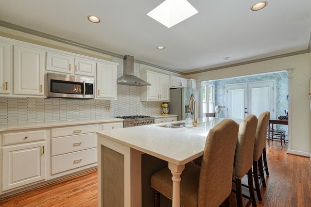 kitchen with wall chimney exhaust hood, stainless steel appliances, crown molding, hardwood / wood-style floors, and a kitchen island with sink