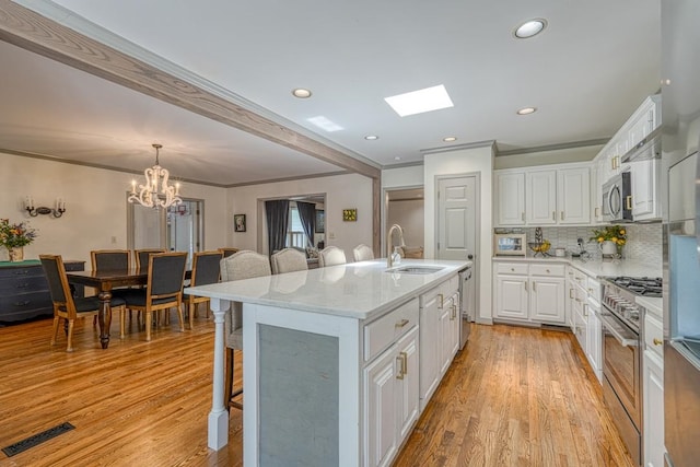 kitchen with sink, light hardwood / wood-style flooring, an island with sink, appliances with stainless steel finishes, and white cabinetry